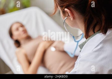 Vue arrière d'une femme médecin examinant le ventre d'une femme enceinte avec stéthoscope à l'hôpital Banque D'Images
