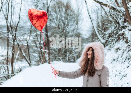 Fille debout sur la route dans la forêt tenant un ballon rouge d'hélium Banque D'Images