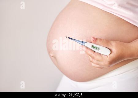 Femme enceinte tenant un thermomètre de fièvre.Traitement de la grippe.Le corps humain.Malade Banque D'Images