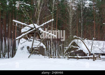 Ancienne maison en bois et moulin à vent recouvert de neige dans une forêt d'hiver. Banque D'Images