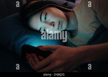 Une femme utilise le téléphone au lit la nuit. Banque D'Images