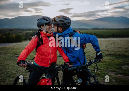 Joyeux couple de cyclistes senior s'embrassant et regardant les uns les autres en plein air dans la nature en automne. Banque D'Images