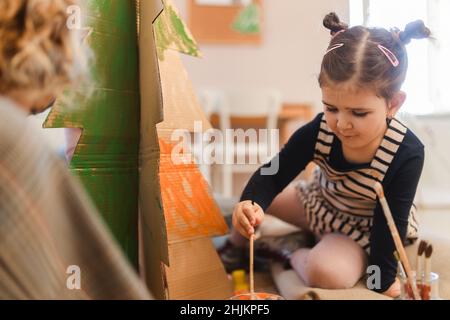 Une petite fille peint un arbre en carton à la classe d'art créatif et d'artisanat à l'école Banque D'Images