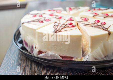 Cheesecake avec gelée de framboise sur un plat noir sur une table en bois.Cheesecake en tranches. Banque D'Images