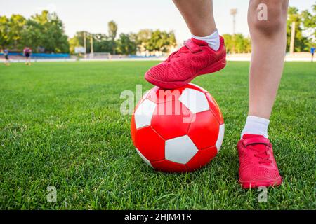 Un garçon se tient sur le terrain de football du stade et tient son pied sur un ballon de football.Les enfants jouent au football sur l'herbe.Formation ou concours co Banque D'Images