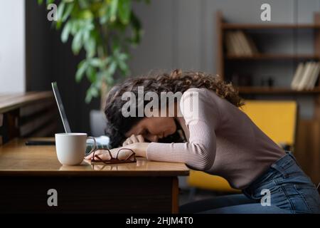 Une femme indépendante fatiguée surtravaillée ou une travailleuse à distance dormant sur un bureau avec un ordinateur portable souffrent de fatigue Banque D'Images