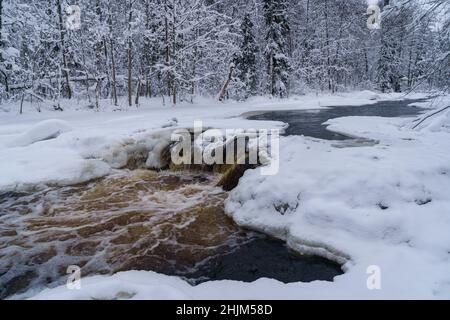 Rivière en cours d'eau non verglaçante dans une forêt enneigée le jour d'hiver sombre et froid Banque D'Images