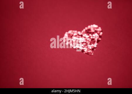 Coeur rouge brillant fait de paillettes sur une table rouge.Copier l'espace Banque D'Images