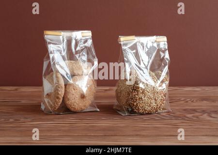 Biscuits aux flocons d'avoine aux graines de sésame et biscuits meringue aux noisettes dans des sacs transparents sur une table en bois contre un mur brun.Gros plan. Banque D'Images