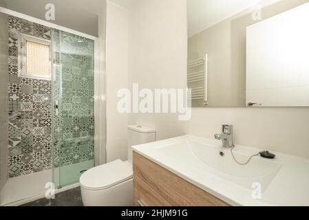 Salle de bains avec lavabo en porcelaine blanche allongé, miroir rectangulaire sans cadre et douche avec cloison en verre et carreaux hydrauliques Banque D'Images