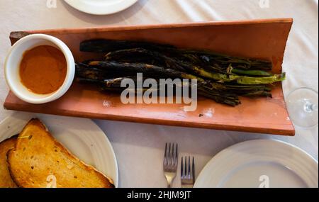 Les oignons calcottes sont servis sur une assiette avec une sauce Romesco - plat traditionnel catalan Banque D'Images