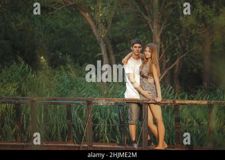 Un beau couple dans la nature se tient enjambant sur un pont en bois au-dessus d'une rivière surcultivée avec des roseaux.Les amoureux heureux fêtent ensemble la Saint-Valentin. Banque D'Images