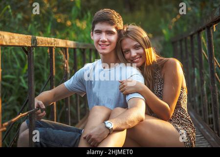 Un gars et une fille sont assis sur un pont en bois au-dessus d'une rivière dans un parc de la ville.Les amoureux s'étreignent dans la nature Banque D'Images