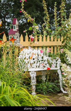 Blanc peint en fonte de style victorien assis contre la clôture de piquetage peinte beige et bordé par le paver rouge - coquelicot, Alcea rosea - Hollyhock. Banque D'Images