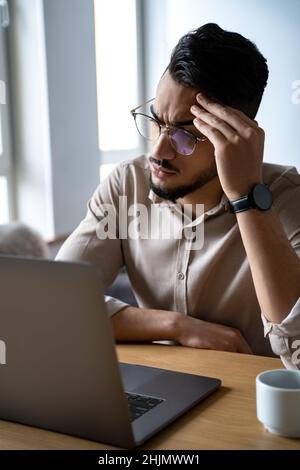 Portrait d'un homme sérieux et perplexe regardant l'écran d'un ordinateur portable assis au bureau Banque D'Images
