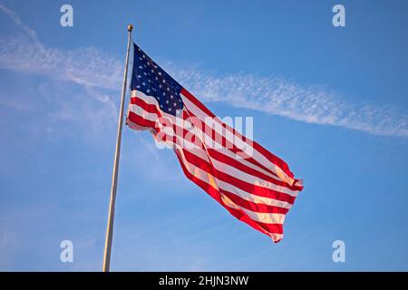 Drapeau américain unique, grand et isolé, volant haut sur un mât contre un ciel bleu clair Banque D'Images