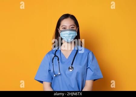 Portrait de studio avec fond orange d'un médecin asiatique avec un masque de visage regardant l'appareil photo Banque D'Images