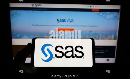 Personne détenant un smartphone avec le logo de la société américaine de logiciels d'analyse SAS Institute Inc. À l'écran devant le site Web.Mise au point sur l'affichage du téléphone. Banque D'Images