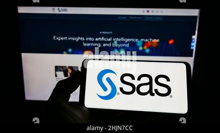 Personne tenant un téléphone portable avec le logo de la société américaine de logiciels d'analyse SAS Institute Inc. À l'écran devant la page Web.Mise au point sur l'affichage du téléphone. Banque D'Images