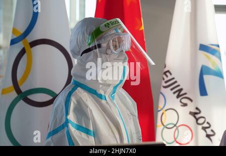 Un membre du personnel de l'aéroport portant un costume de noisette se trouve à côté d'un drapeau olympique à l'aéroport international de Beijing alors que les passagers débarquent un vol après leur arrivée en vue des Jeux Olympiques d'hiver de 2022 à Beijing en Chine.Date de la photo: Lundi 31 janvier 2022. Banque D'Images