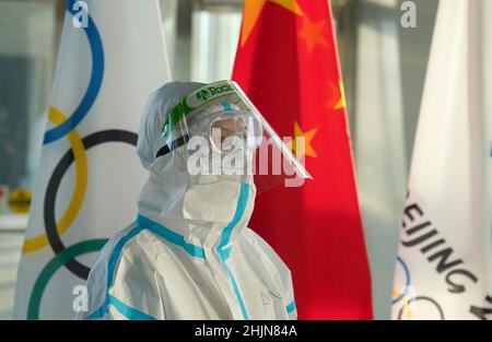 Un membre du personnel de l'aéroport portant un costume de noisette se trouve à côté d'un drapeau olympique à l'aéroport international de Beijing alors que les passagers débarquent un vol après leur arrivée en vue des Jeux Olympiques d'hiver de 2022 à Beijing en Chine.Date de la photo: Lundi 31 janvier 2022. Banque D'Images