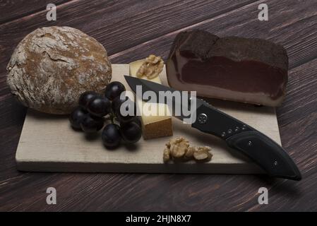 Savoureux loin bacon fromage raisins noix pain traditionnel du Tyrol du Sud et couteau à grignoter sur une planche en bois clair devant un backgroun en bois sombre Banque D'Images