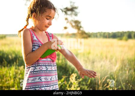 Une fille pulvérise des moustiques sur la peau dans la nature qui mord ses mains et ses pieds.Protection contre les piqûres d'insectes, répulsif sans danger pour les enfants.recr. Extérieure Banque D'Images