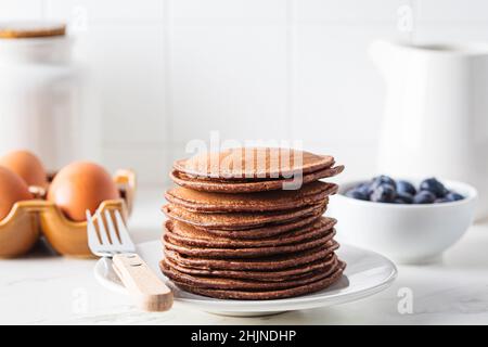 Crêpes au chocolat sur une assiette blanche et ingrédients pour cuisiner dans la cuisine blanche. Banque D'Images