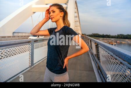 YYoung souriante femme en forme se reposant après un entraînement actif de fitness en plein air dans la ville Banque D'Images