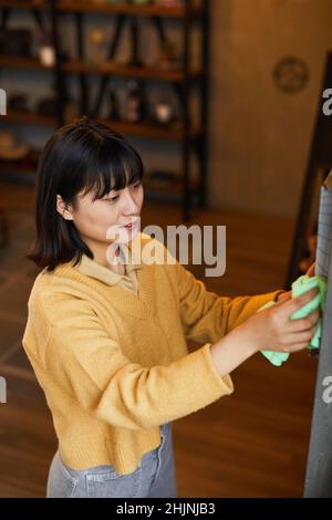Portrait vertical de la jeune femme asiatique qui nettoie et dépoussiérage à la maison Banque D'Images