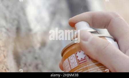 Gros plan de l'artiste dessine des œuvres d'art de rue pulvérisant de la peinture.Action.Les doigts tachés de l'artiste tiennent la bombe avec de la peinture colorée sur le mur en béton.Rue Banque D'Images