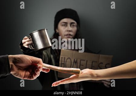 L'homme donne une pile d'argent à la femme, les mains rapprochées.La mendicité défocuée tient une affiche en carton avec le texte sans-abri sur l'arrière-plan.La conce Banque D'Images