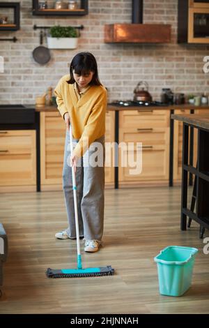 Portrait vertical de la jeune femme asiatique qui lave les sols tout en nettoyant un appartement confortable Banque D'Images