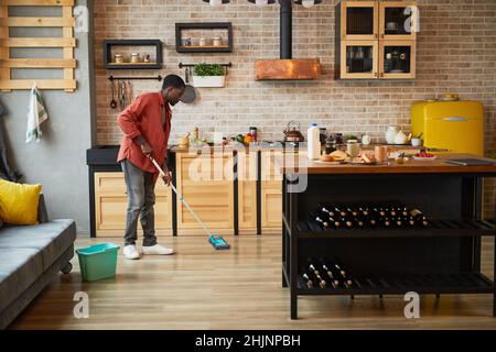Grand angle de vue sur les jeunes Afro-américains homme de laver les sols tout en nettoyant confortable appartement, espace de copie Banque D'Images