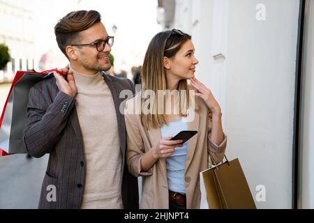Beau jeune couple aimant portant des sacs d'achats et appréciant ensemble Banque D'Images