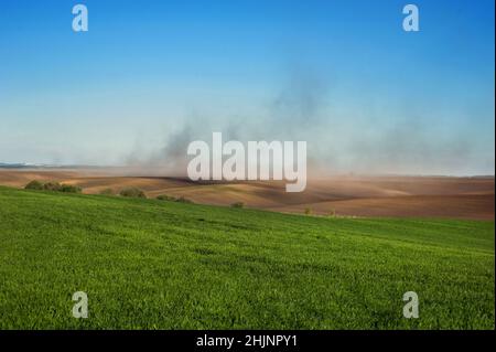 nuages de poussière sur les collines des terres labourées, champs verts blé d'hiver et problème d'érosion du sol par le vent Banque D'Images