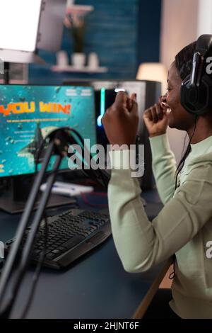 Une joueuse pro joueuse gagnante excitée joue en ligne des jeux vidéo gagnant un tournoi de tir spatial.Un joueur qui a réussi à parler avec des lecteurs à distance lors d'une discussion en streaming à l'aide du clavier RVB dans un studio à domicile Banque D'Images