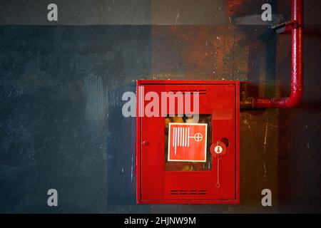 Tuyau d'incendie dans une boîte rouge.Rouleau de tuyau pour urgence incendie dans armoire métallique rouge sur le mur de béton peint à l'huile grise avec des réflexions multicolores comme partie de feu Banque D'Images