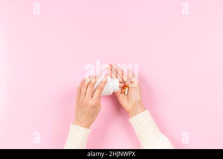 Pilules et capsules de médecine colorées dans la main de femme sur fond rose pastel.Les pilules de déversement de main de femme hors de la pharmacie de bouteille blanche, médecine et Banque D'Images