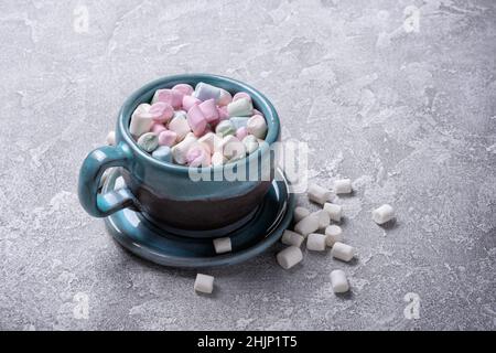 Grande tasse bleue avec mini guimauves colorées pour chocolat chaud, cacao, fête sur fond de béton gris Banque D'Images