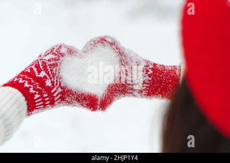 Les mains des femmes en moufles tricotées avec coeur de neige en hiver.Concept de jour d'amour ou de Saint-Valentin Banque D'Images