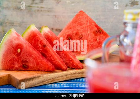 Vue normale de certains triangles de pastèque fraîche avec une partie d'un verre au premier plan hors foyer.Des aliments sains, frais et naturels.Fruits de saison Banque D'Images