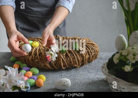 Femme faisant une couronne florale de Pâques de matériaux naturels, fleurs et oeufs colorés. Atelier de printemps. Banque D'Images