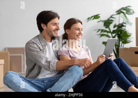 Heureux heureux couple millénaire caucasien assis parmi les boîtes et les plantes dans la chambre à l'intérieur et de faire un appel vidéo Banque D'Images