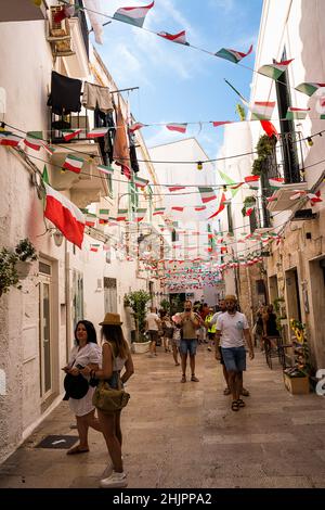 Monopoli, Italie - 20 août 2021 : allée caractéristique avec drapeaux suspendus et touristes dans le centre de Monopoli (Puglia) Banque D'Images