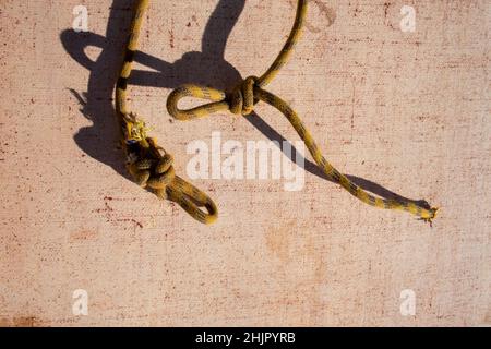 Corde jaune abandonnée et nouée avec ombres sur fond texturé Banque D'Images