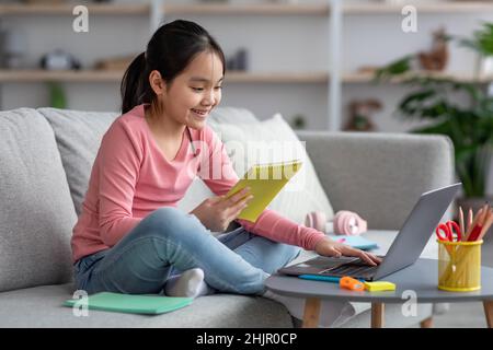 Bonne fille asiatique qui fait ses devoirs à l'aide d'un ordinateur portable Banque D'Images