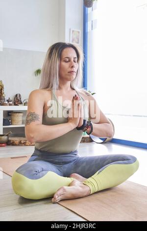 Jeune femme sportive attrayante pratiquant le yoga, faisant de l'exercice Ardha Padmasana, méditant dans la moitié de la posture du Lotus avec le namaste, s'entraîner. Banque D'Images