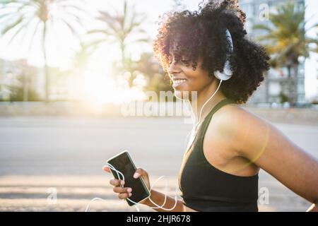 une femme noire avec des cheveux afro s'exécute à écouter de la musique sur la plage Banque D'Images