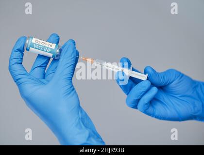 Vaccination contre le covid-19.Un médecin portant des gants bleus tient une seringue et une ampoule avec un vaccin. Banque D'Images